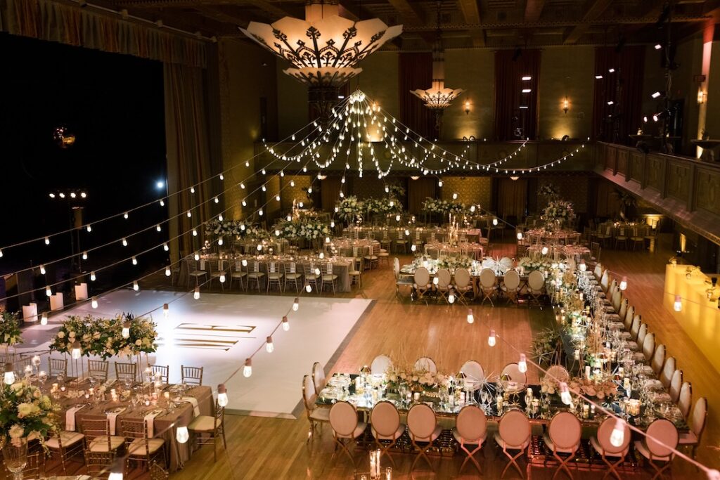 Elegant wedding reception with string lights, floral arrangements, and banquet tables set in a grand ballroom ambiance.