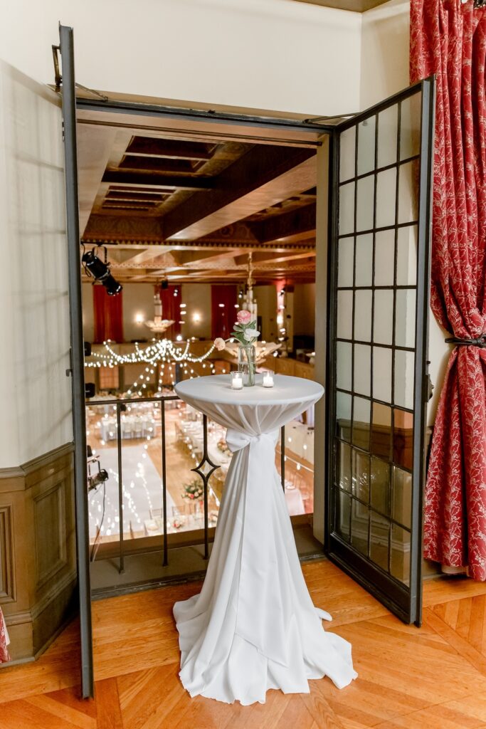 Elegant wedding balcony view with decorated cocktail table overlooking a beautifully lit ballroom.