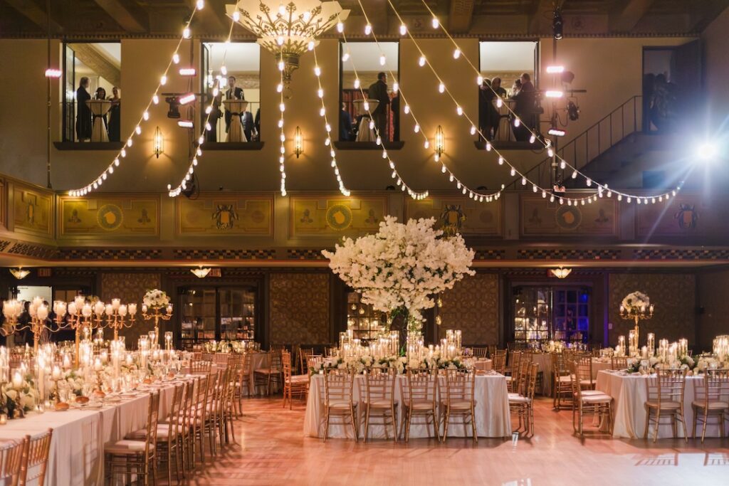 Elegant ballroom decorated with flowers and string lights set for a wedding reception.