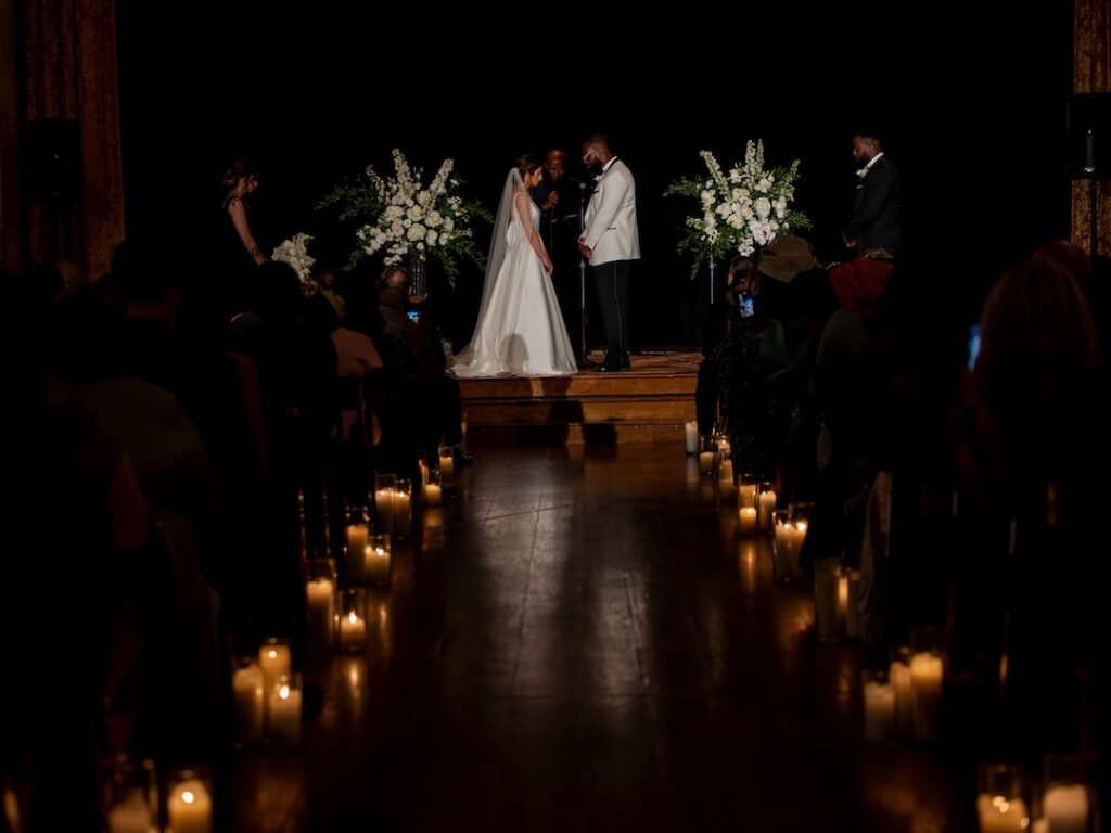 Elegant wedding ceremony with bride and groom exchanging vows, surrounded by candles and floral arrangements.