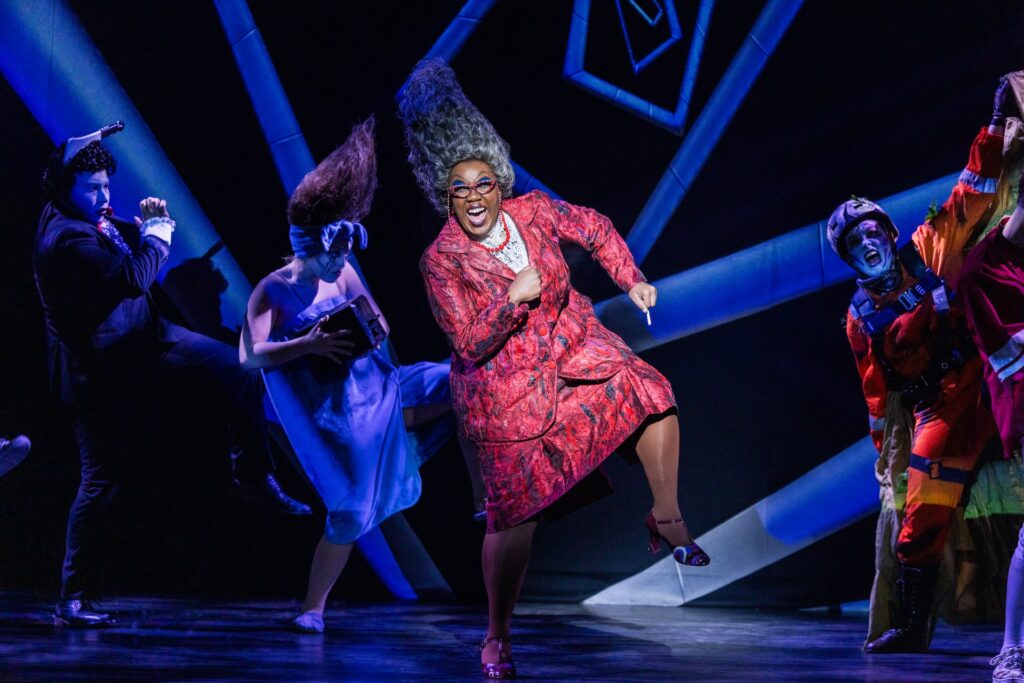 Performer in vibrant costume dances energetically on stage during a theatrical production.