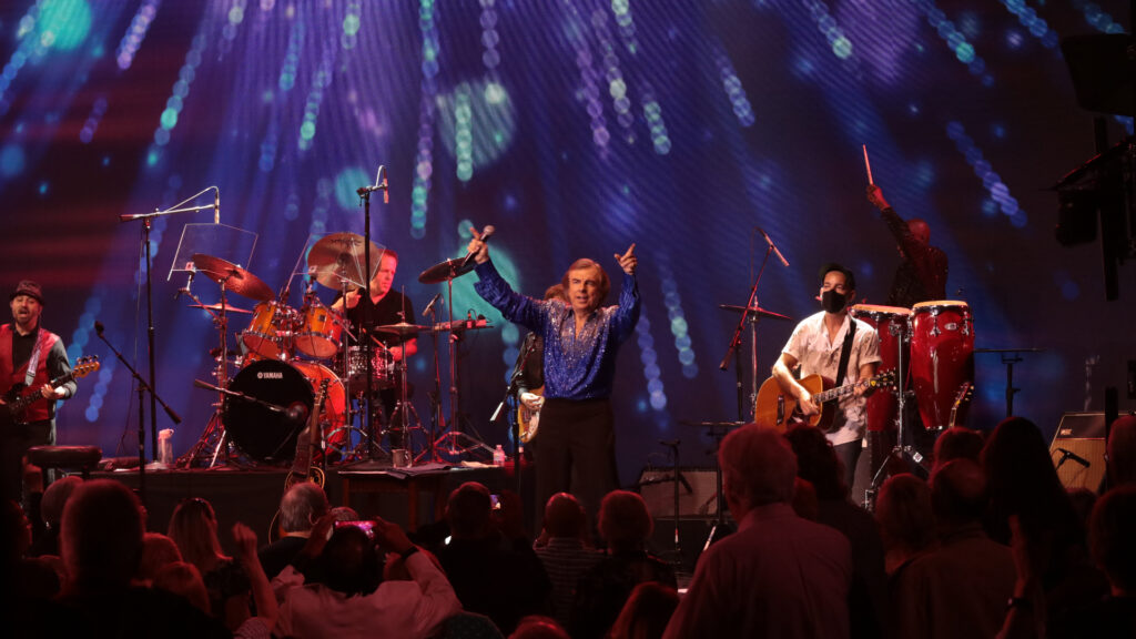 Live band performing on stage with vibrant lights and enthusiastic audience.